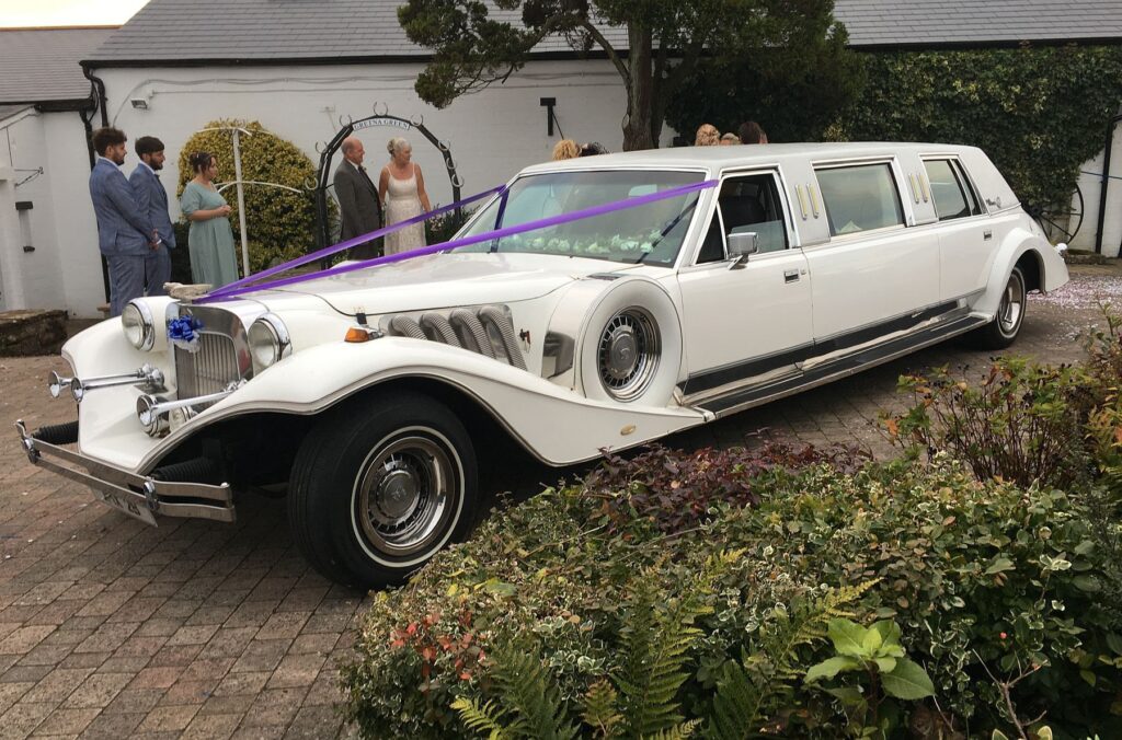 A White, hotrod style limo at a wedding venue.