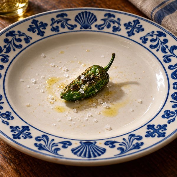 Pementos de Herbón. A single green pepper on a blue and white plate.